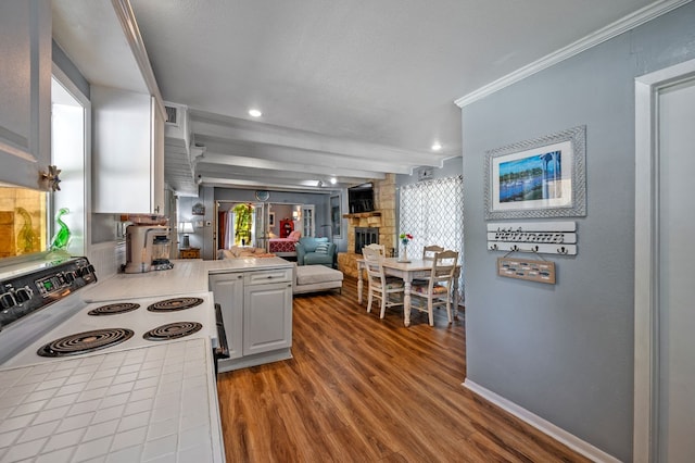 kitchen with tile counters, white cabinets, a stone fireplace, and hardwood / wood-style flooring