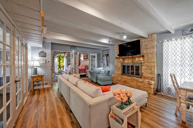 living room featuring french doors, a stone fireplace, hardwood / wood-style flooring, and beamed ceiling