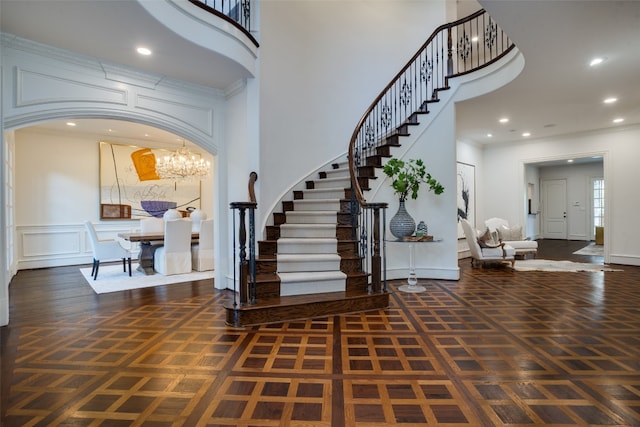 entryway with dark parquet flooring, a notable chandelier, and a towering ceiling