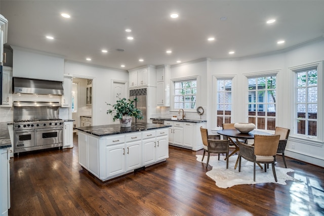 kitchen with stainless steel appliances, dark wood-type flooring, wall chimney exhaust hood, white cabinets, and backsplash