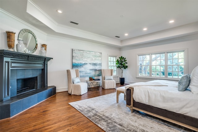 bedroom with a tile fireplace, dark wood-type flooring, and a tray ceiling