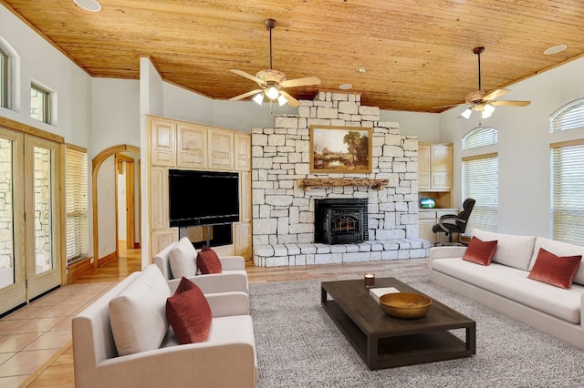 tiled living room featuring a towering ceiling, wooden ceiling, ceiling fan, and a stone fireplace