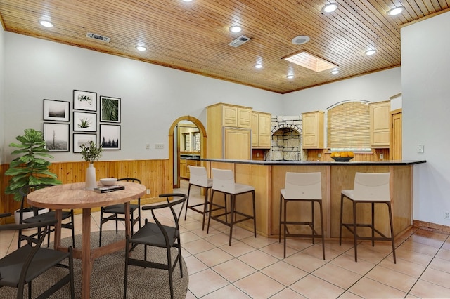 kitchen featuring a kitchen breakfast bar, tasteful backsplash, kitchen peninsula, and light tile floors