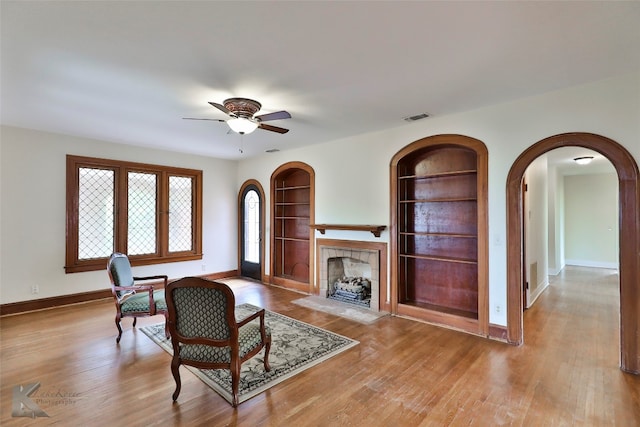 living area featuring ceiling fan, built in shelves, and light wood-type flooring