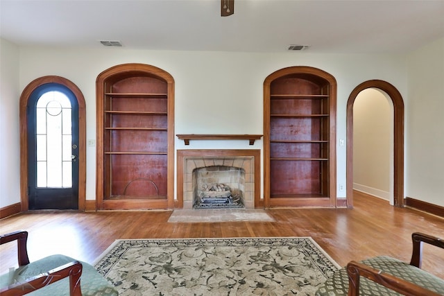 unfurnished living room with built in features, light wood-type flooring, and a fireplace