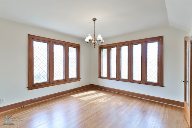 unfurnished room with lofted ceiling, light hardwood / wood-style floors, and a notable chandelier