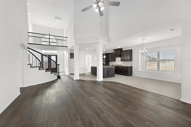 unfurnished living room with ceiling fan with notable chandelier, dark hardwood / wood-style floors, and a high ceiling