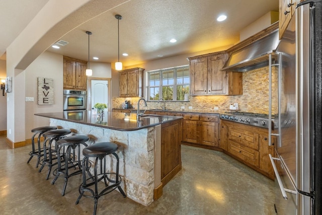 kitchen with decorative light fixtures, a kitchen bar, stainless steel appliances, a center island with sink, and tasteful backsplash