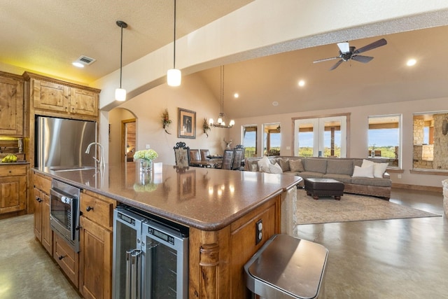 kitchen featuring pendant lighting, ceiling fan with notable chandelier, beverage cooler, a center island with sink, and appliances with stainless steel finishes