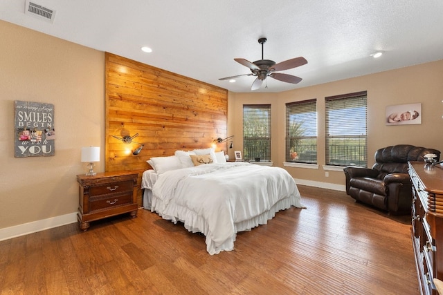 bedroom featuring wooden walls, ceiling fan, dark wood-type flooring, and a textured ceiling