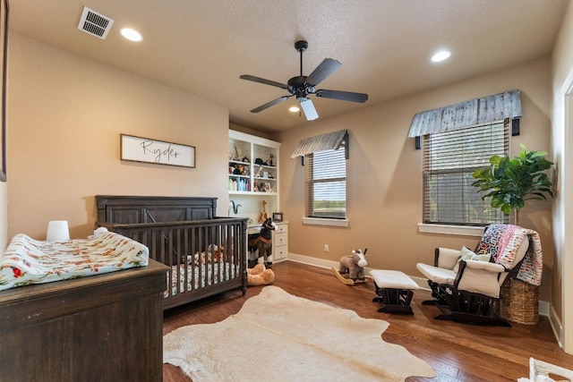 bedroom with a fireplace, a crib, ceiling fan, a textured ceiling, and dark hardwood / wood-style floors