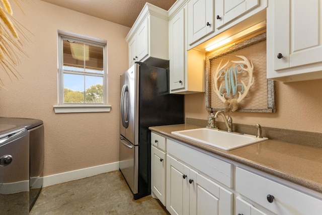 kitchen with stainless steel fridge, sink, a textured ceiling, white cabinetry, and washing machine and dryer