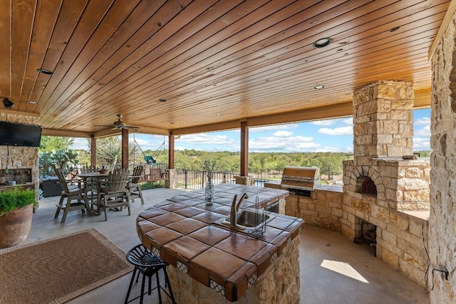 view of terrace featuring exterior kitchen, grilling area, an outdoor stone fireplace, and ceiling fan