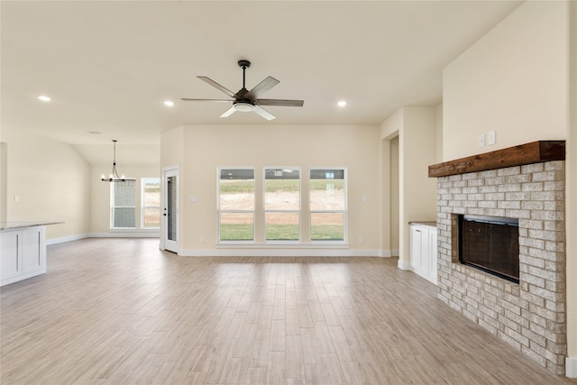 unfurnished living room with a brick fireplace, ceiling fan with notable chandelier, and light hardwood / wood-style flooring