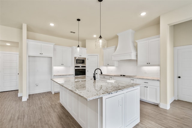 kitchen with white cabinetry, premium range hood, decorative light fixtures, a center island with sink, and appliances with stainless steel finishes