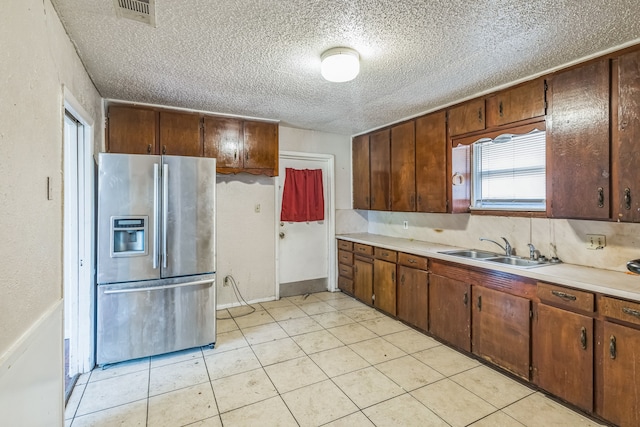 kitchen with light tile patterned flooring, a textured ceiling, sink, and stainless steel fridge with ice dispenser