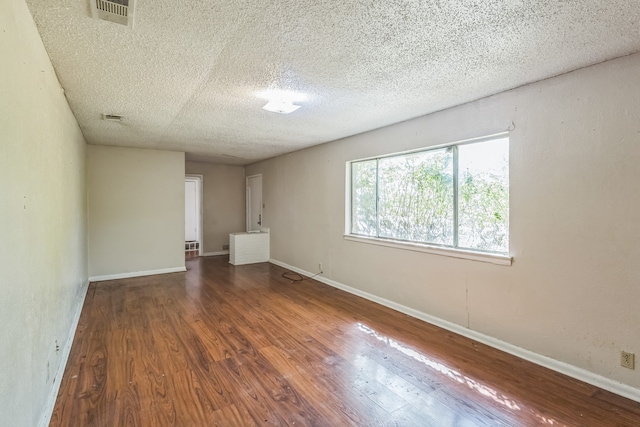 empty room with a textured ceiling and dark hardwood / wood-style flooring