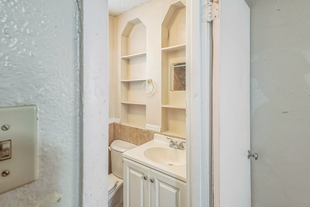 bathroom with a textured ceiling, built in features, toilet, and vanity