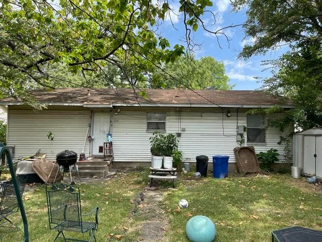 back of property featuring a lawn and a storage shed