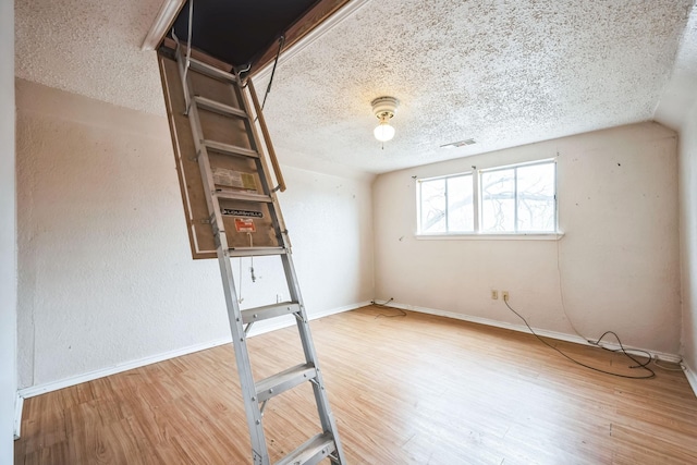 spare room with a textured ceiling, vaulted ceiling, and wood-type flooring