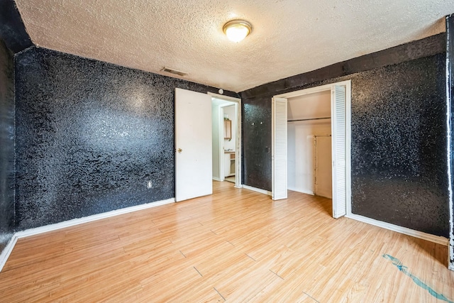 unfurnished bedroom with wood-type flooring, a closet, and a textured ceiling