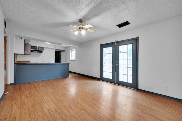 unfurnished living room featuring ceiling fan, light hardwood / wood-style flooring, french doors, and a textured ceiling