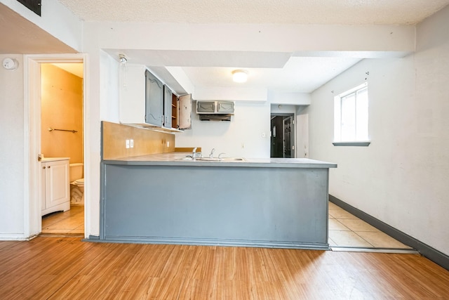 kitchen with sink, a textured ceiling, light hardwood / wood-style floors, and kitchen peninsula