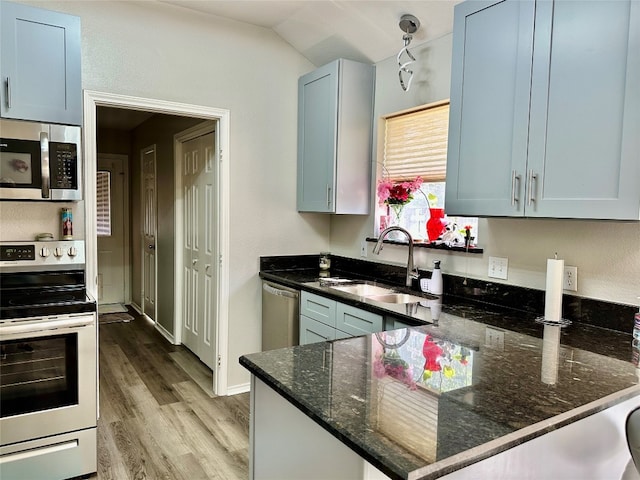 kitchen with appliances with stainless steel finishes, dark stone countertops, vaulted ceiling, sink, and light hardwood / wood-style flooring