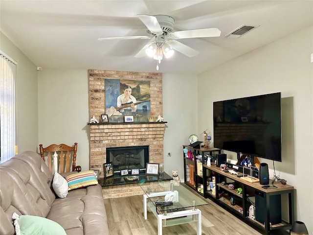 living room with light hardwood / wood-style flooring, ceiling fan, brick wall, and a brick fireplace