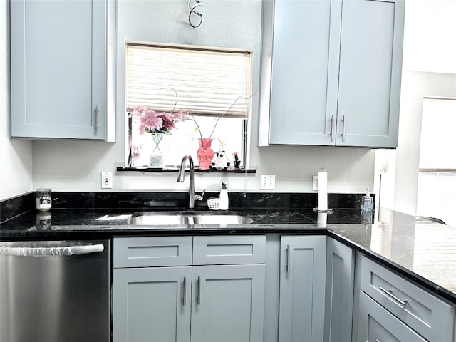 kitchen with stainless steel dishwasher, sink, dark stone counters, and gray cabinetry