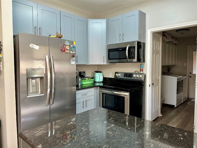 kitchen featuring dark hardwood / wood-style flooring, stainless steel appliances, dark stone countertops, and washer and clothes dryer