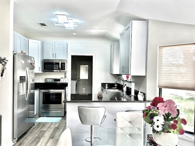 kitchen featuring dark stone counters, appliances with stainless steel finishes, a kitchen bar, light hardwood / wood-style flooring, and lofted ceiling