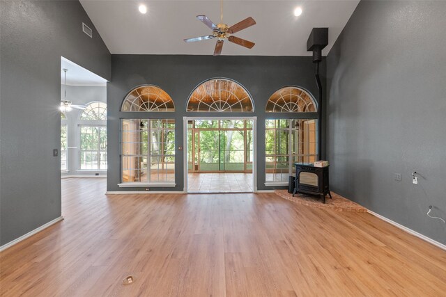 unfurnished living room with a wood stove, high vaulted ceiling, ceiling fan, and light wood-type flooring