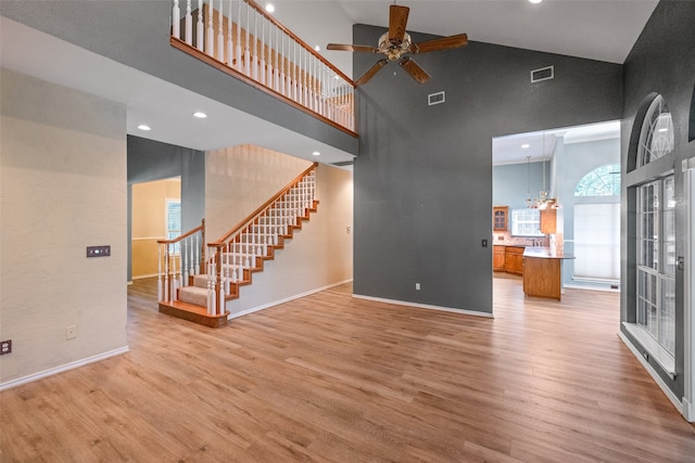 unfurnished living room with ceiling fan with notable chandelier, high vaulted ceiling, and hardwood / wood-style flooring