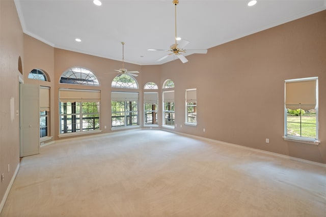 carpeted spare room with ornamental molding, ceiling fan, and a towering ceiling