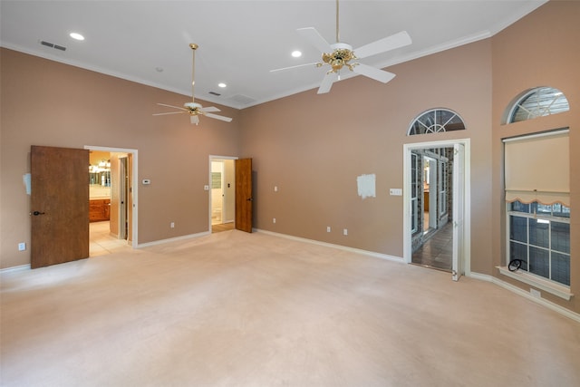 unfurnished living room with light colored carpet, ornamental molding, ceiling fan, and a towering ceiling