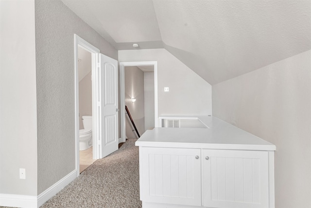 corridor featuring light carpet, a textured ceiling, and vaulted ceiling