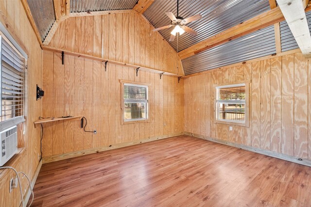 unfurnished room featuring ceiling fan, light hardwood / wood-style flooring, wooden walls, and plenty of natural light