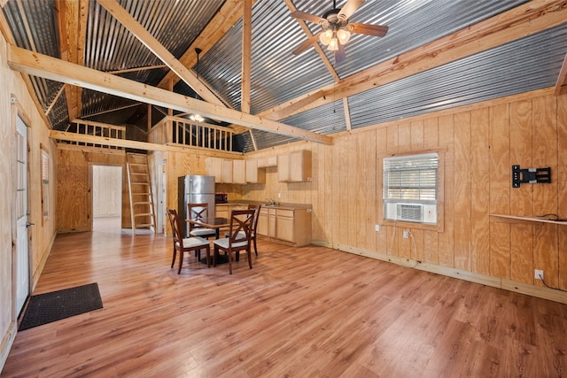 dining area featuring ceiling fan, wooden walls, light hardwood / wood-style floors, sink, and lofted ceiling with beams