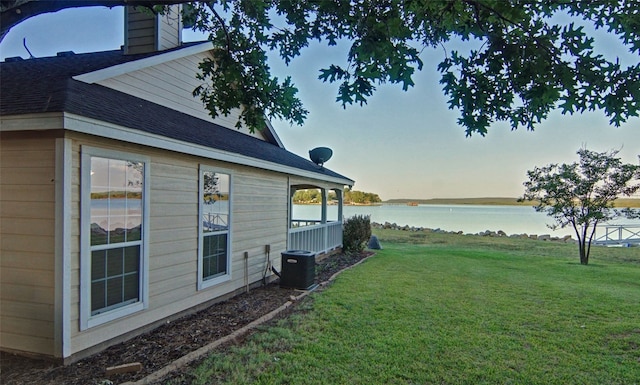 property exterior at dusk with a water view, central AC, and a lawn