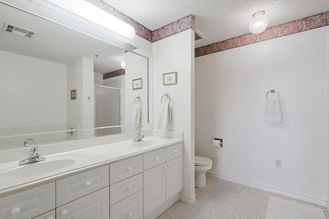 bathroom with a textured ceiling, double sink, toilet, and vanity with extensive cabinet space