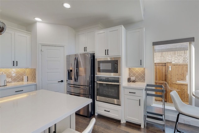 kitchen with dark hardwood / wood-style flooring, backsplash, white cabinetry, and appliances with stainless steel finishes