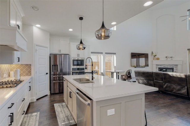 kitchen featuring decorative light fixtures, appliances with stainless steel finishes, a stone fireplace, a center island with sink, and backsplash