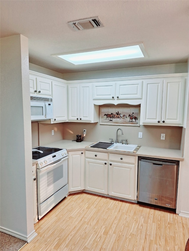 kitchen featuring white appliances, white cabinetry, a skylight, sink, and light wood-type flooring