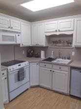 kitchen with white appliances, light hardwood / wood-style floors, sink, and white cabinetry