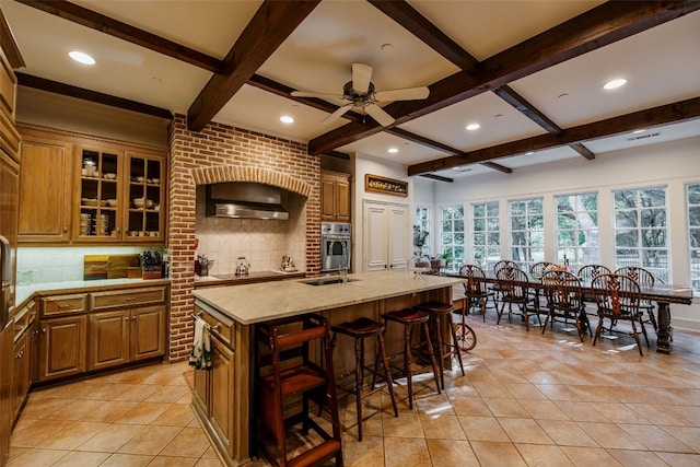 kitchen with a center island with sink, beam ceiling, tasteful backsplash, and ceiling fan