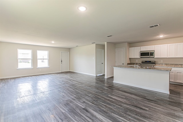 kitchen with white cabinetry, dark hardwood / wood-style flooring, light stone counters, a center island with sink, and stove