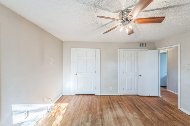 unfurnished bedroom featuring multiple closets, ceiling fan, hardwood / wood-style floors, and a textured ceiling