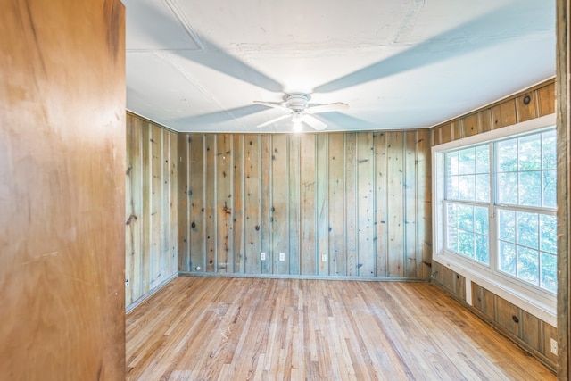 empty room with light wood-type flooring, wood walls, and ceiling fan