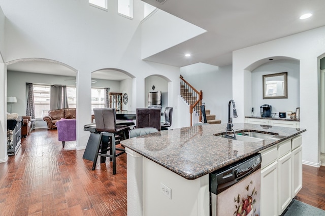 kitchen featuring a kitchen island with sink, white cabinets, sink, and dark stone counters